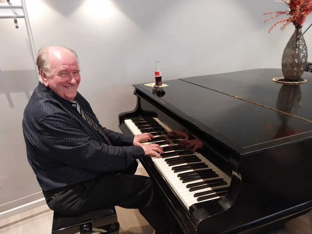 Pianist Jos Lermyte lacht breed terwijl hij aan een zwarte vleugel speelt