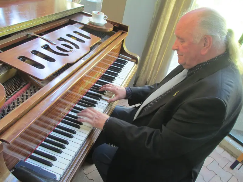 Jos Lermyte speelt op een klassieke houten vleugel bij het raam